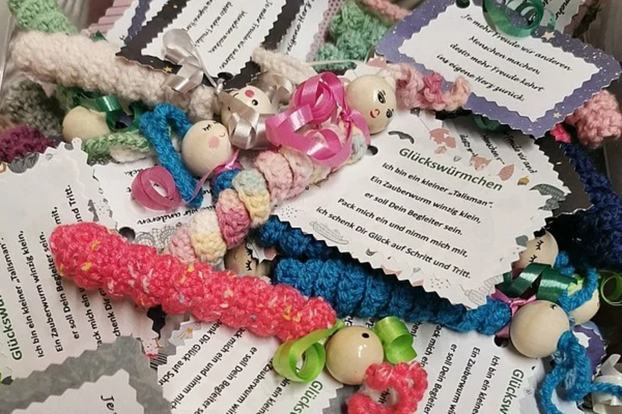Bunte gehäkelte Glücksbringer mit Holzperlenköpfen und kleinen Schleifen, an jedem ein beschriftetes Kärtchen mit Sprüchen.