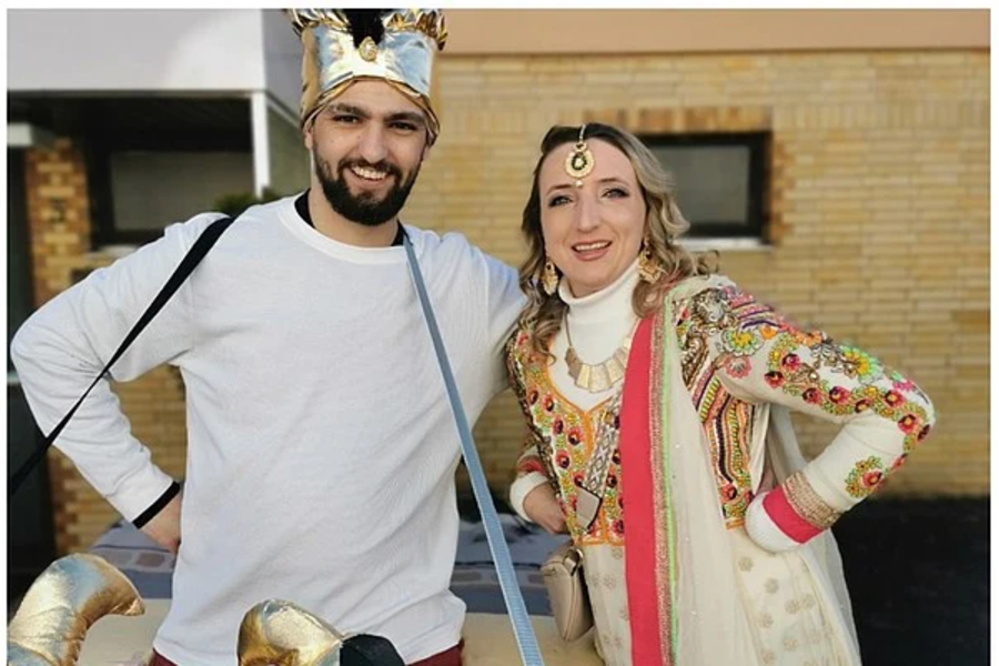 Oben zwei Personen in Kostümen, eine trägt weiße Kleidung mit goldenen Hörnern, die andere ein buntes, traditionelles Kleid mit roten und goldenen Mustern. Unten eine Kiste voller bunter Snackverpackungen.